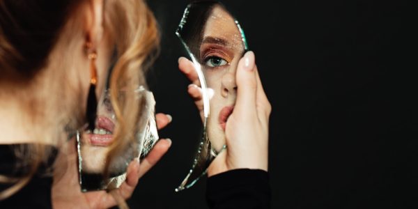 Serious woman looking at broken self-image mirror on black background lady looking at broken mirror
